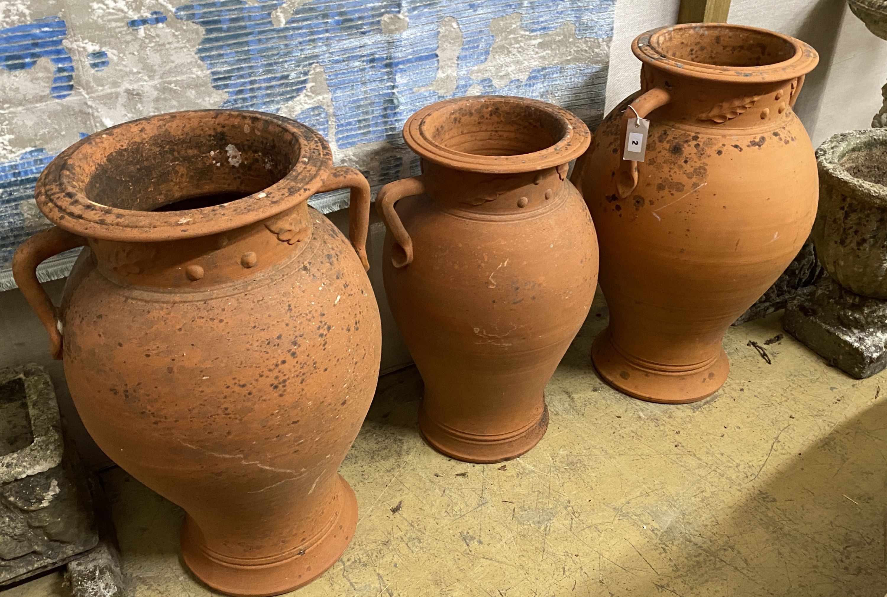 A set of three terracotta baluster garden urns moulded with leaves, largest height 72cm